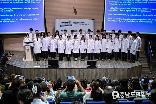 Photo 2: The first cohort of medical students participating in the White Coat Ceremony and taking the Hippocratic Oath